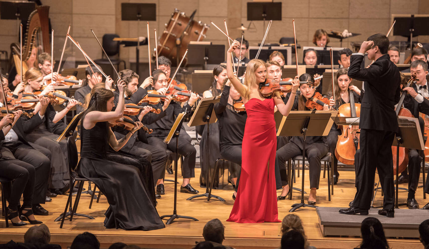 A symphony performs while a violin soloist plays in the center wearing a red dress