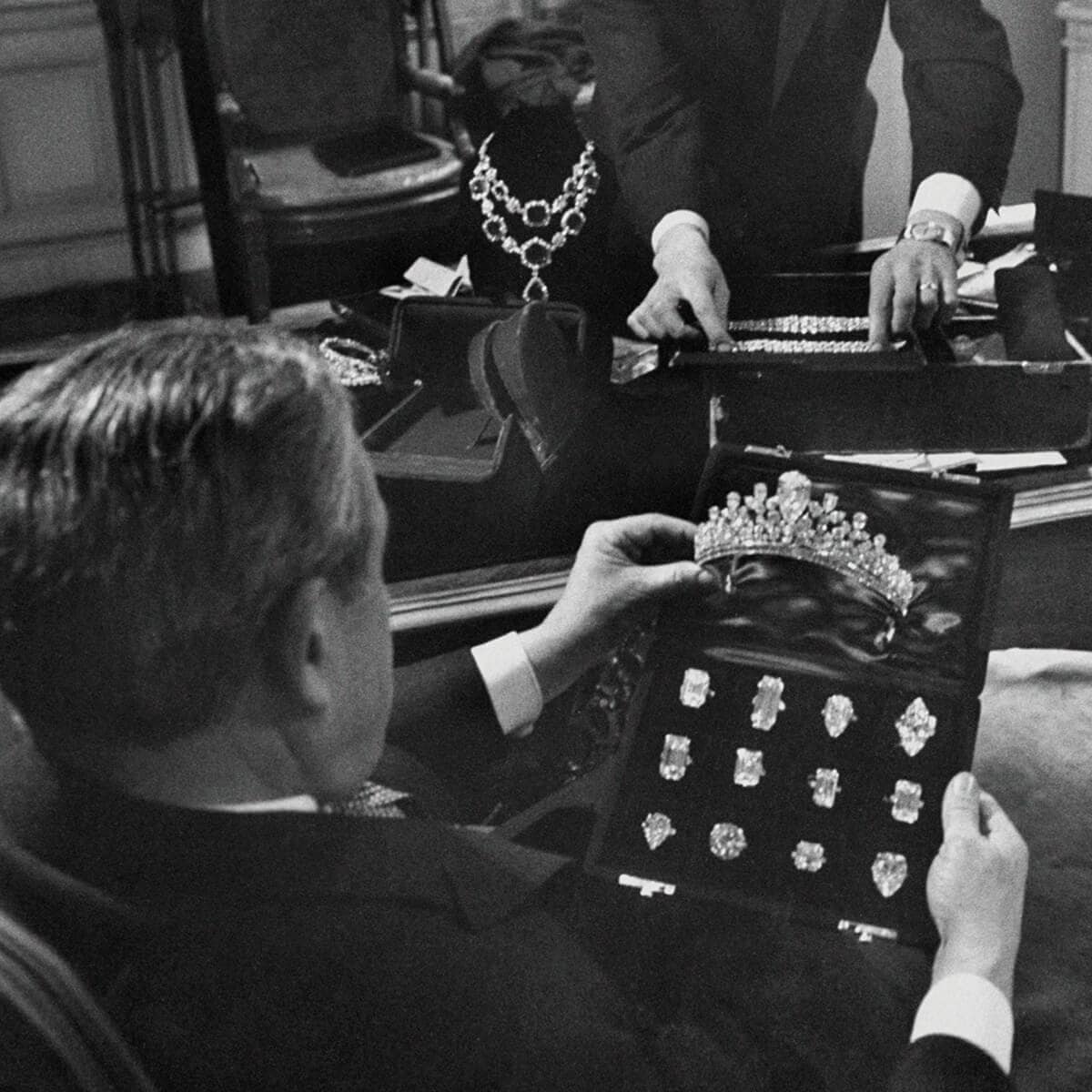 A black and white image of Mr. Winston at his desk with a variety of diamond rings and a diamond tiara